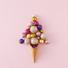 Top view photo of christmas tree balls flying out of ice cream cone on isolated pastel pink background. Minimal Christmas holiday concept background.