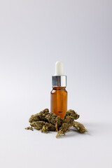 Vertical image of bottle of cbd oil and dried marihuana leaves on white surface