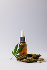 Vertical image of bottle of cbd oil and marihuana leaf on white surface