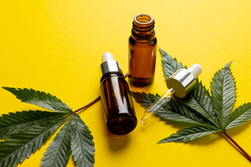 Image of bottle of cbd oil and marihuana leaves on yellow surface