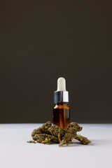 Vertical image of bottle of cbd oil and dried marihuana leaves on grey surface