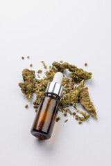 Vertical image of bottle of cbd oil and dried marihuana leaves on white surface