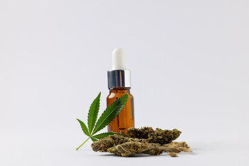 Image of bottle of cbd oil and dried marihuana leaves on white surface