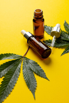 Vertical image of bottle of cbd oil and marihuana leaves on yellow surface