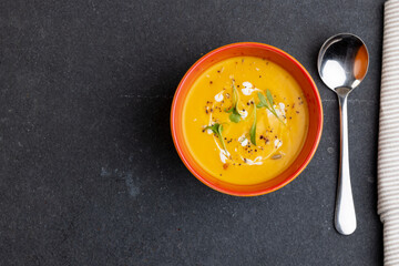 Horizontal image of bowl of tomato soup with garnish, and napkin on slate, copy space