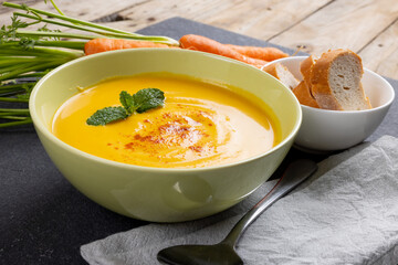 Horizontal image of bowl of carrot soup with garnish, raw carrots and sliced bread on slate