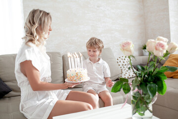 Happy woman and boy celebrating the child birthday at home. The kid blows out the candles in the birthday cake