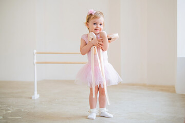 Portrait of a cute blue-eyed baby ballerina in pink hugging pointe shoes.