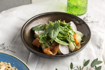 Salmon salad with radish, cucumber and greens on brown plate on the table