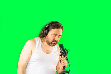 A shocked unshaven man in a white undershirt speaks into a microphone. Unemployed slovenly dressed man from Eastern Europe.