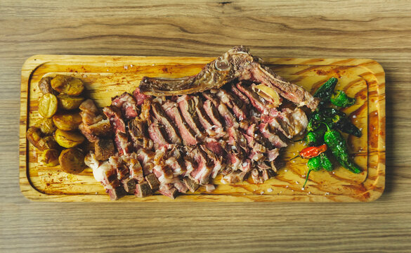 Juicy and appetizing sliced beef meat steak with potatoes and Padron peppers. Spanish Chuleton de Ternera. Grilled meat at wooden cutting board. Top view image