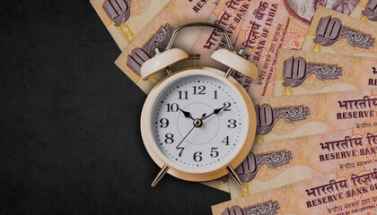 Alarm clock on indian ten rupees notes on black background, time to invest,, loan, business and insurance idea
