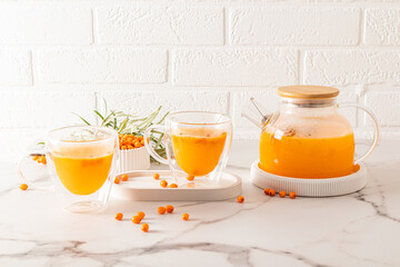 hot seasonal vitamin tea from sea buckthorn in glass cups and a kettle on a white marble table opposite the brick wall.