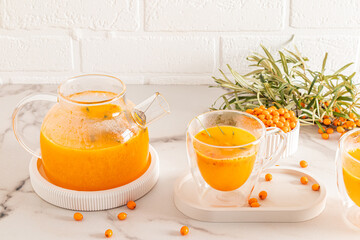 a large glass teapot with hot traditional seasonal sea buckthorn tea and a tea-filled cup. the concept of health promotion, vitamins.