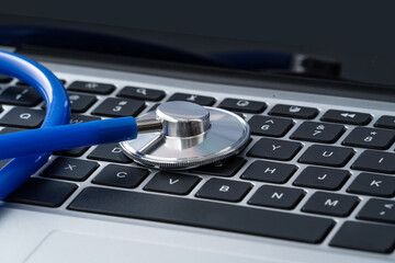 Blue stethoscope on laptop computer keyboard, medical design concept.