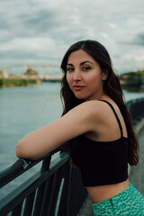 Portrait of a beautiful young brunette on the bridge by the river