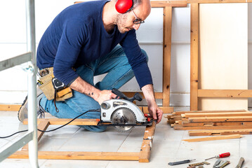 carpenter working kneeling cutting wood with electric machine and tool belt
