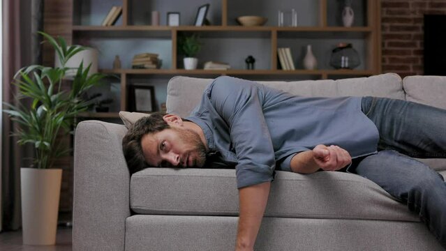 Tired man collapses on the couch, feeling apathetic. Feeling depressed, lack of motivation, sadness, boredom. Exhausted, he collapses on the couch from the stress. Burnout