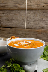 Vertical image of cream pouring into bowl of tomato soup, with wood background and copy space