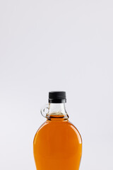 Vertical image of glass bottle of maple syrup on white background, with copy space