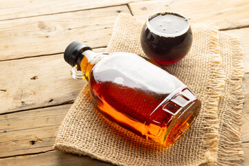 Horizontal image of glass bottle and bowl of maple syrup on sackcloth on wooden table © vectorfusionart