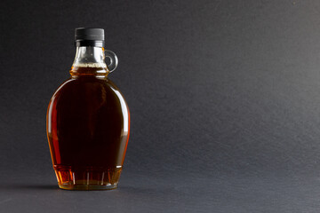 Horizontal image of glass bottle of maple syrup on dark grey background, with copy space