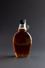 Vertical image of glass bottle of maple syrup on dark grey background, with copy space