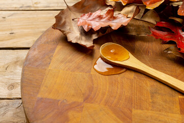 Horizontal image of autumn leaves and wooden spoon of maple syrup on wood, with copy space