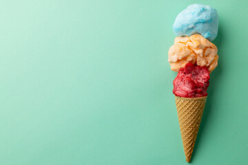 Horizontal image of three coloured flavours of ice cream in cone, on blue background with copy space