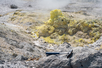 geological hammer on the rock against the backdrop of an steaming fumarole on the slope of a volcano
