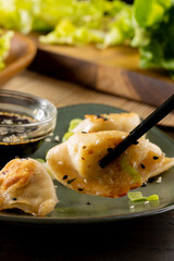 Close up of asian dumplings, soy sauce and chopsticks on plate on wooden background