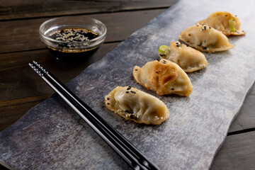 Close up of asian dumplings, soy sauce and chopsticks with slate and wooden background