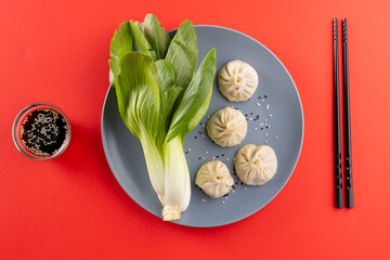 Overhead view of asian dumplings, soy sauce, endive and chopsticks on red background