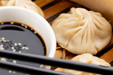 Close up of asian steamed dumplings, soy sauce and chopsticks in wooden dish