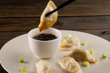 Gordijnen Close up of asian dumplings, soy sauce and chopsticks on plate and wooden background © vectorfusionart
