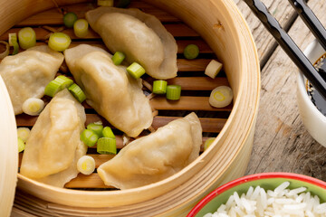Close up of asian dumplings, soy sauce, rice and chopsticks in wooden dish and wooden background