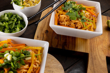Close up of asian wok stir fry noodles with chopsticks and condiments on wooden boards
