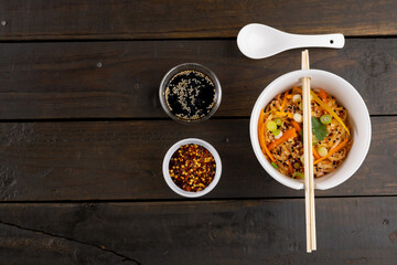 Overhead view of asian wok stir fry noodles and chopsticks and condiments on wooden background