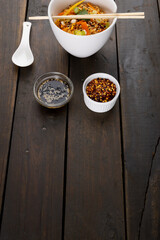 Close up of asian wok stir fry noodles and chopsticks and condiments on wooden background
