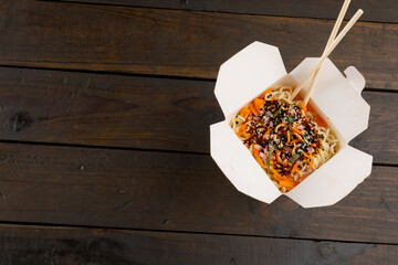 Overhead view of take away asian wok stir fry noodles with chopsticks in paper container on wood