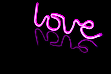 Image of vibrant neon love text formed with pink glow sticks over black background and copy space