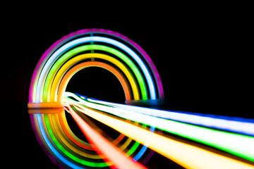 Image of vibrant neon glow sticks forming rainbow over black background with copy space