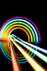 Image of vibrant neon glow sticks forming rainbow over black background with copy space