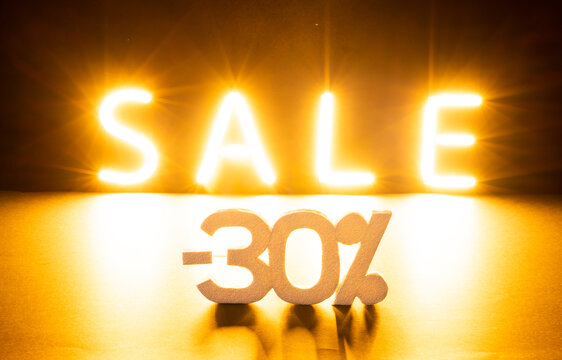 Image of glowing neon minus 30 percent sale text over orange background