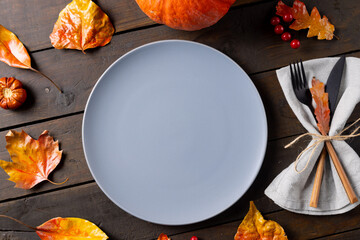 Overhead view of plate and cutlery in napkin with autumn decoration, copy space on wooden background