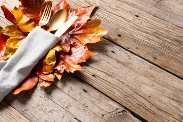 Overhead view of cutlery in napkin with autumn decoration and copy space on wooden background