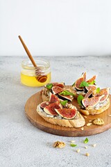 Crispy bruschetta (toast) with soft ricotta, ripe figs, walnuts and pine nuts, mint and honey on a...