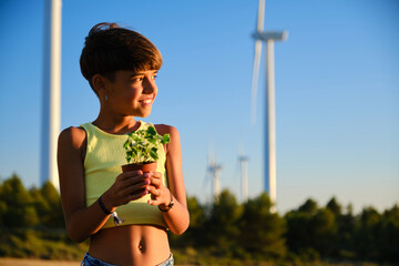 Young girl looking away and smiling while holding a plant standing outdoors in the field.