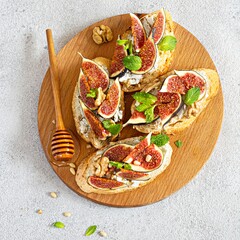 Crispy bruschetta (toast) with soft ricotta, ripe figs, walnuts and pine nuts, mint and honey on a...