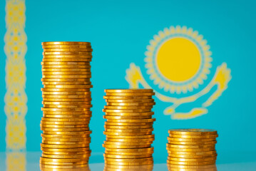 Three stacks of gold coins from highest to lowest near flag of Kazakhstan. Financial crisis in Kazakhstan symbol